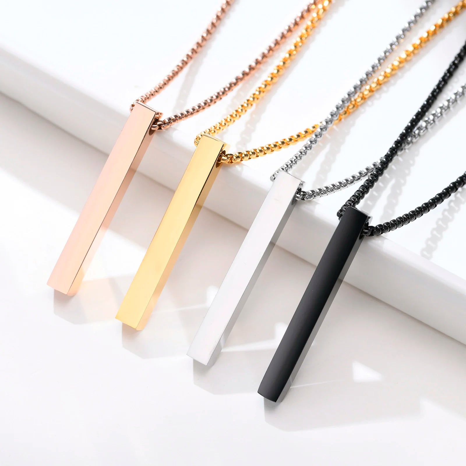 Pendant necklace in rose gold, gold, silver, and black finishes laid flat side by side