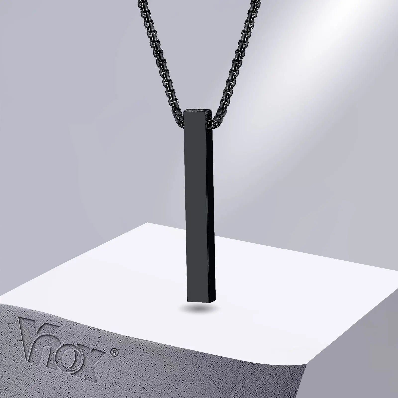 Black stainless steel pillar pendant necklace displayed on a white stone stand